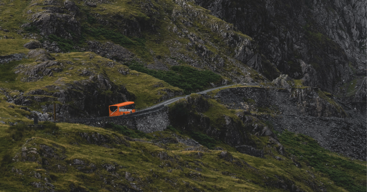 A red coach driving up a steep rural road in England