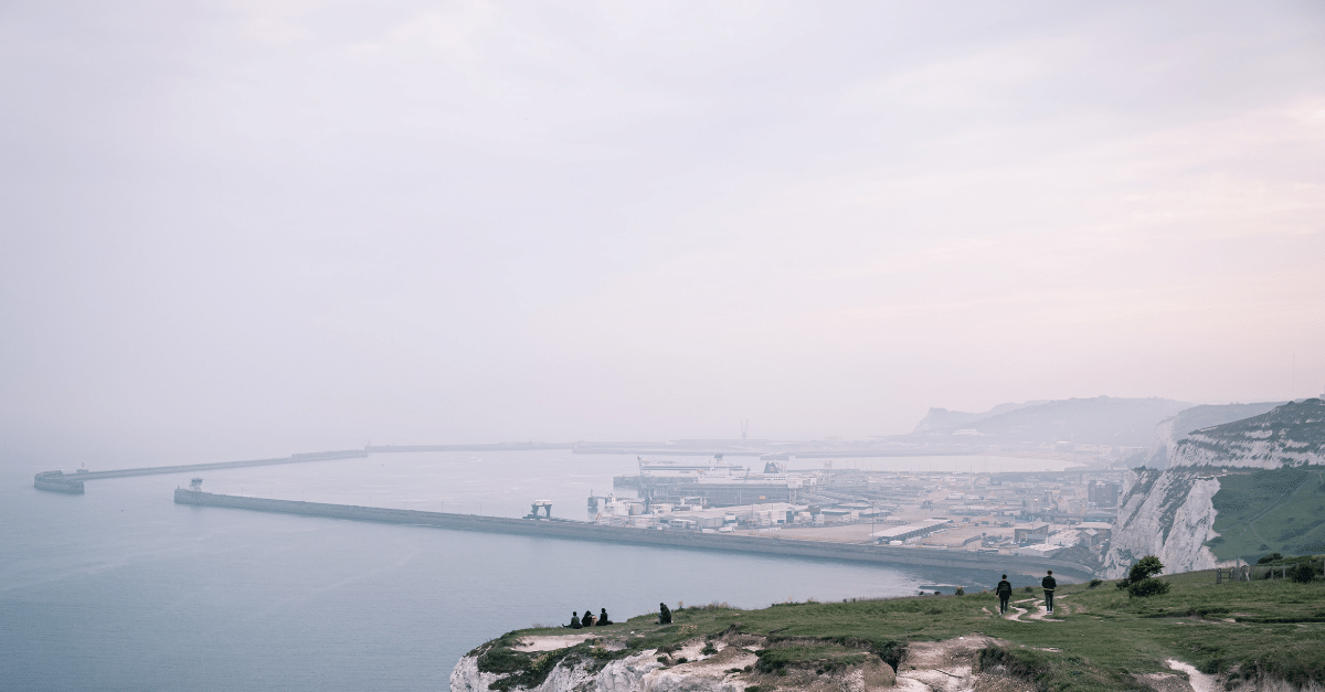 Group of people sitting at the top of the Dover cliffs overlooking the sea on a foggy day